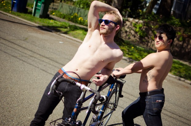two shirtless men next to a tandem bicycle